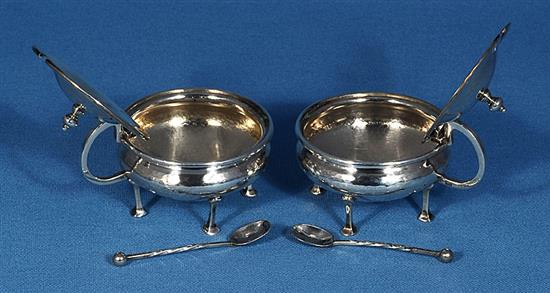 A pair of George V Arts & Crafts silver mustard pots with matching spoons, by Albert Edward Jones, width 90mm, weight 5.1oz/160grms.